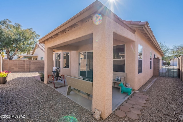 rear view of house featuring stucco siding, fence, and a patio