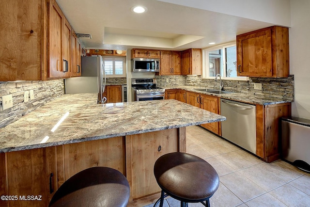 kitchen featuring a tray ceiling, a sink, visible vents, appliances with stainless steel finishes, and brown cabinetry