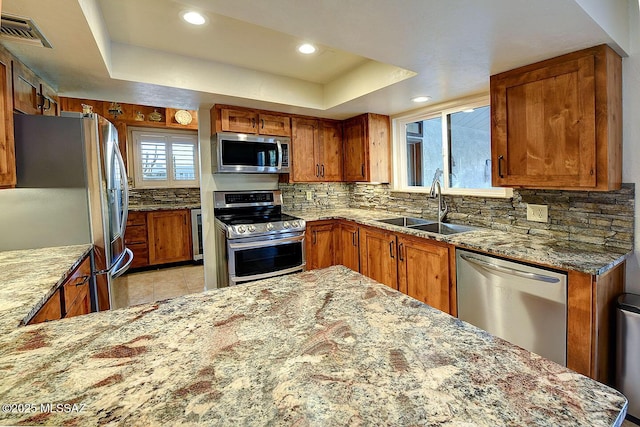kitchen featuring a tray ceiling, a sink, light stone countertops, appliances with stainless steel finishes, and visible vents