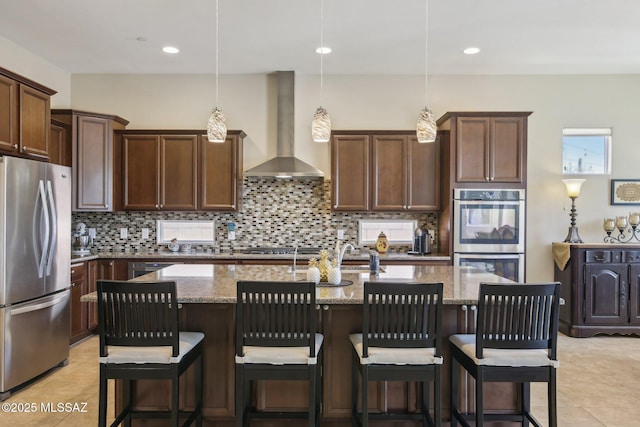 kitchen with light tile patterned floors, light stone countertops, wall chimney range hood, appliances with stainless steel finishes, and decorative backsplash