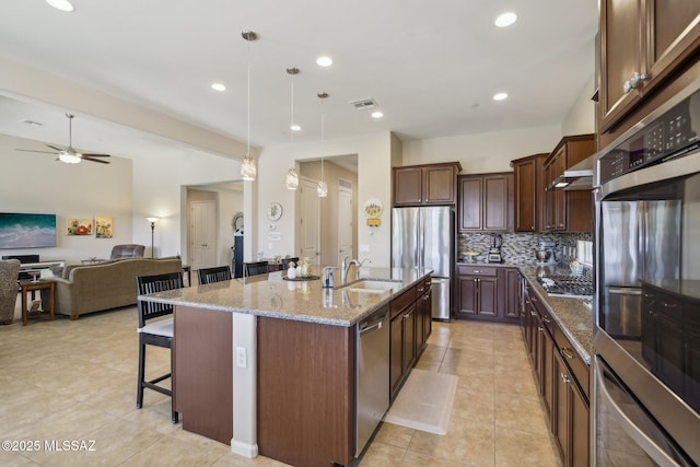 kitchen featuring a breakfast bar, light stone countertops, visible vents, appliances with stainless steel finishes, and a sink