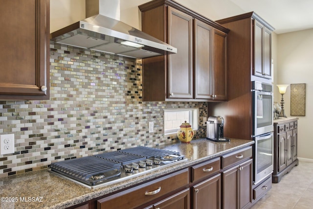 kitchen with dark stone countertops, wall chimney exhaust hood, backsplash, and stainless steel appliances