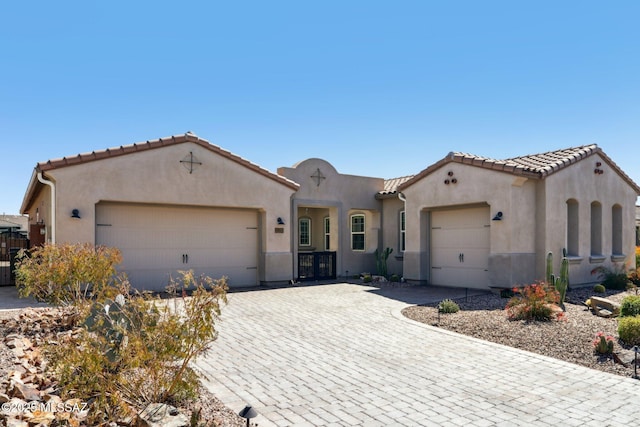 mediterranean / spanish-style home featuring driveway, stucco siding, an attached garage, and a tile roof