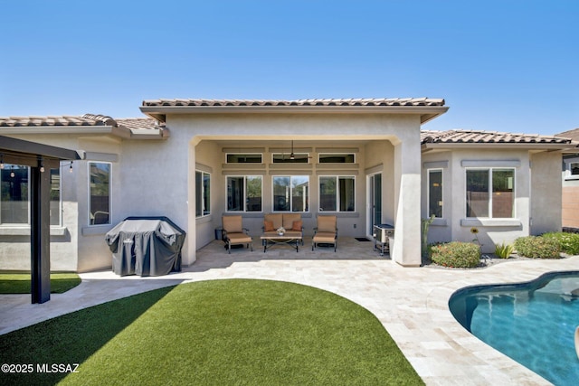 back of house with stucco siding, a lawn, a patio area, a tile roof, and an outdoor pool