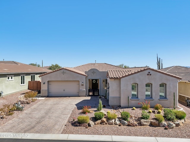 mediterranean / spanish-style house featuring an attached garage, stucco siding, a tile roof, and decorative driveway