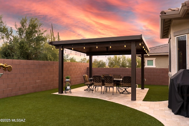 patio terrace at dusk featuring a yard, a fenced backyard, and a grill