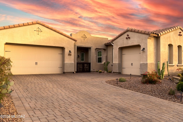 mediterranean / spanish-style home featuring a garage, stucco siding, a tile roof, and decorative driveway