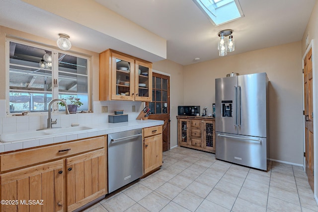 kitchen featuring a skylight, a sink, glass insert cabinets, appliances with stainless steel finishes, and backsplash