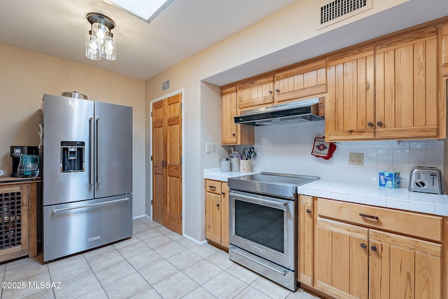 kitchen featuring under cabinet range hood, stainless steel appliances, tasteful backsplash, and visible vents