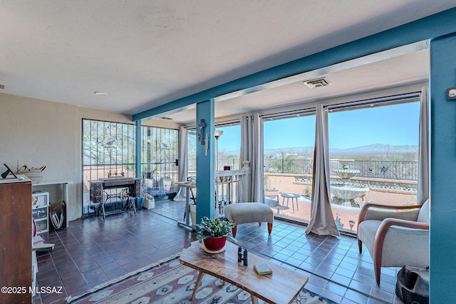 living area with tile patterned floors, visible vents, a mountain view, and a textured wall