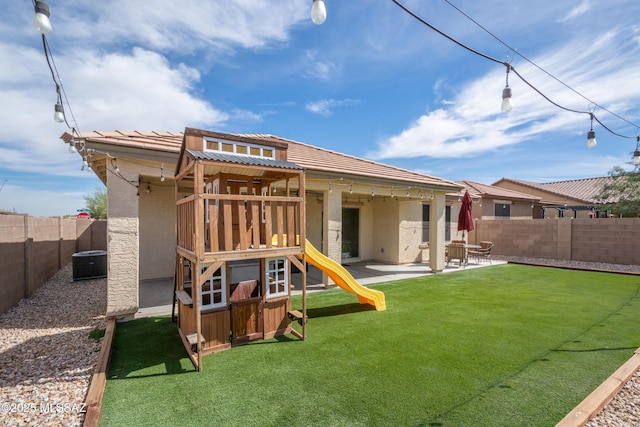 back of house featuring stucco siding, a patio, a fenced backyard, a playground, and a lawn