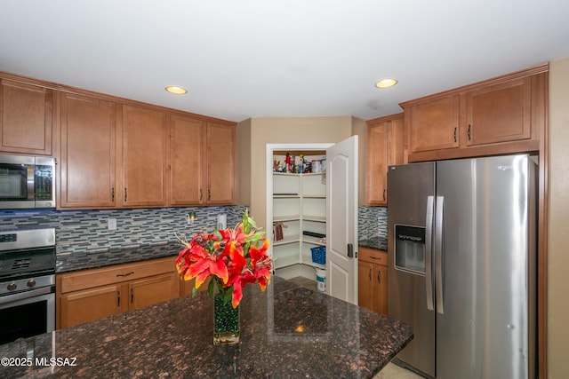 kitchen featuring dark stone countertops, appliances with stainless steel finishes, brown cabinets, and decorative backsplash