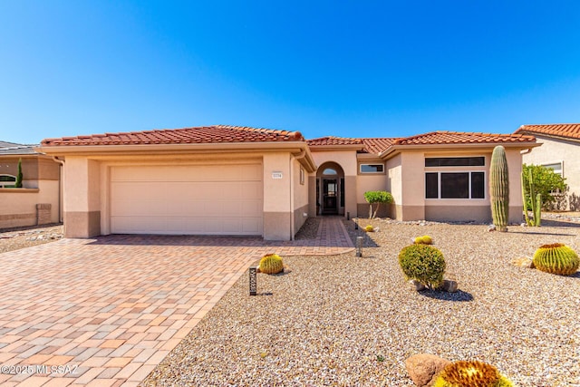 mediterranean / spanish house featuring stucco siding, a garage, a tiled roof, and decorative driveway