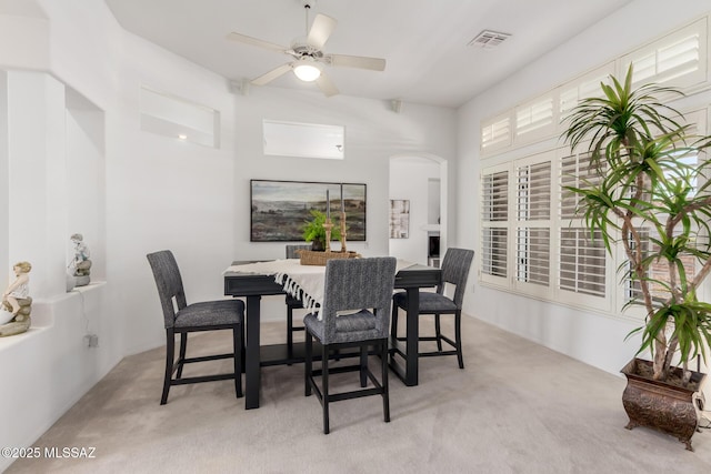 dining room featuring arched walkways, light carpet, ceiling fan, and visible vents
