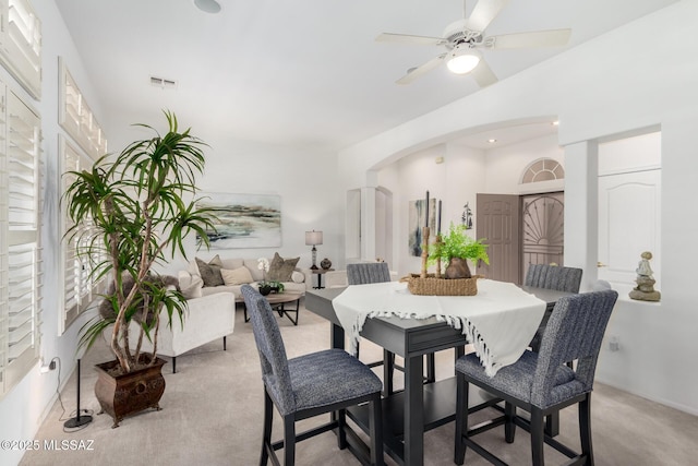 carpeted dining area featuring visible vents, arched walkways, and a ceiling fan