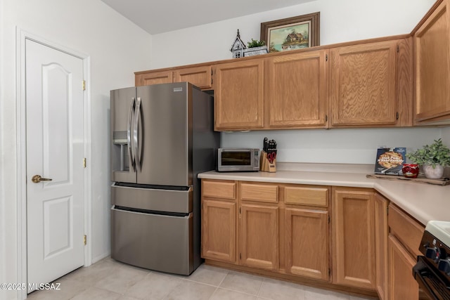 kitchen with light countertops, stainless steel refrigerator with ice dispenser, light tile patterned floors, range, and brown cabinetry