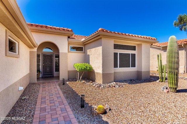 view of exterior entry with stucco siding and a tiled roof
