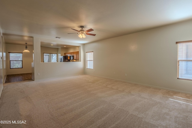 unfurnished living room featuring a healthy amount of sunlight, ceiling fan, baseboards, and light carpet