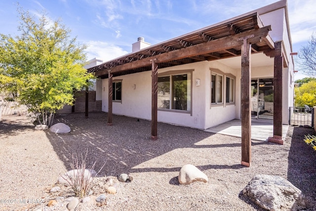 rear view of house featuring stucco siding, fence, and a patio area