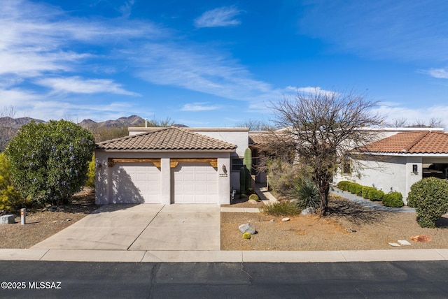view of front facade with stucco siding, a tile roof, a mountain view, concrete driveway, and a garage