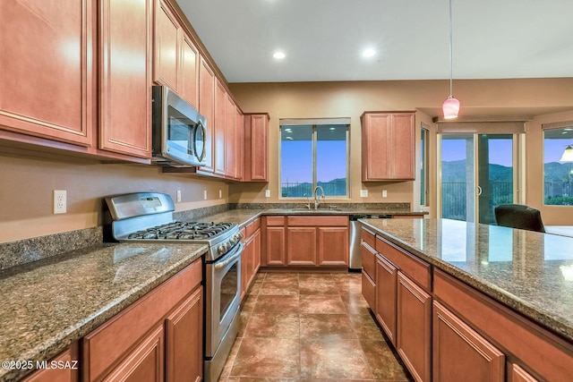 kitchen featuring recessed lighting, appliances with stainless steel finishes, dark stone countertops, a sink, and decorative light fixtures