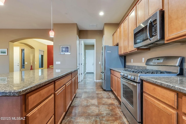 kitchen with decorative light fixtures, dark stone counters, visible vents, appliances with stainless steel finishes, and brown cabinetry