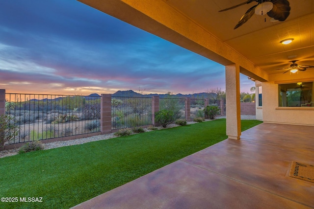 patio terrace at dusk featuring a fenced backyard, a ceiling fan, and a yard