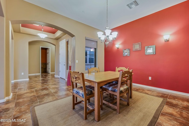 dining space featuring a notable chandelier, a raised ceiling, baseboards, visible vents, and arched walkways