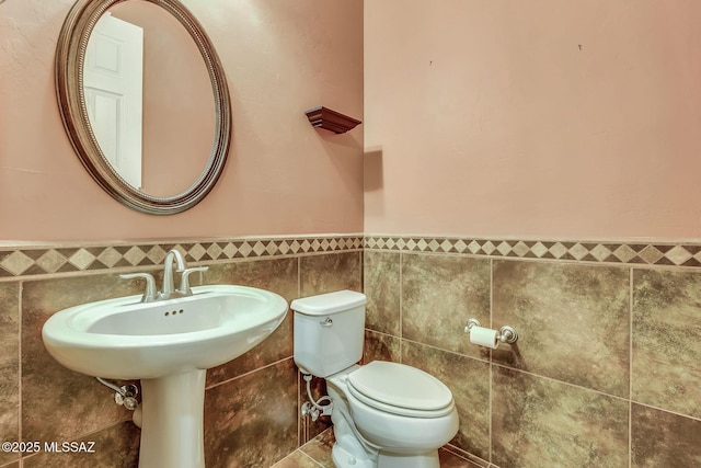bathroom featuring toilet, a wainscoted wall, and tile walls