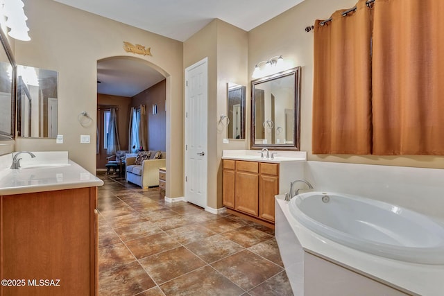 full bath with a sink, two vanities, baseboards, and a garden tub