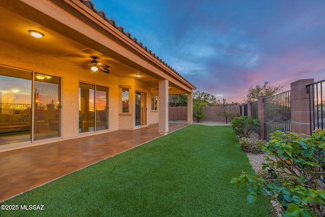 yard at dusk with a fenced backyard, ceiling fan, and a patio area