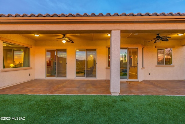 rear view of house with a ceiling fan, stucco siding, a yard, and a patio