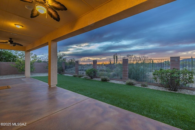 patio terrace at dusk with a fenced backyard, a yard, and ceiling fan
