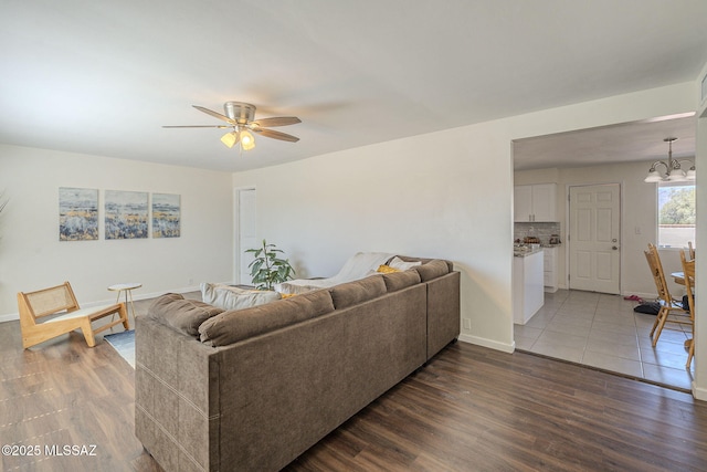living room featuring dark wood finished floors, baseboards, and ceiling fan with notable chandelier