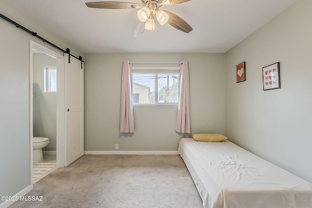 carpeted bedroom with a barn door, ceiling fan, ensuite bath, and baseboards