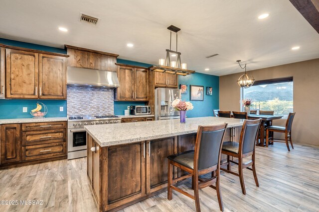 kitchen with visible vents, a kitchen island, ventilation hood, a chandelier, and stainless steel appliances