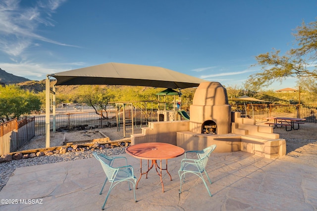 view of patio / terrace featuring a mountain view, a fireplace, playground community, and fence