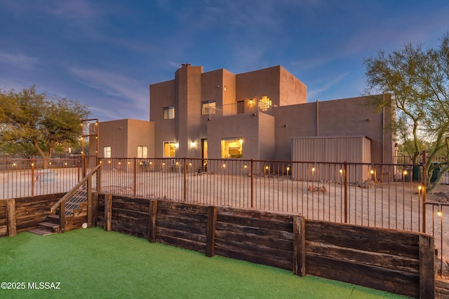 back of property at dusk with fence and stucco siding
