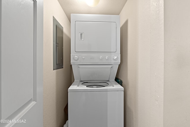laundry room with laundry area, electric panel, a textured wall, and stacked washer and clothes dryer