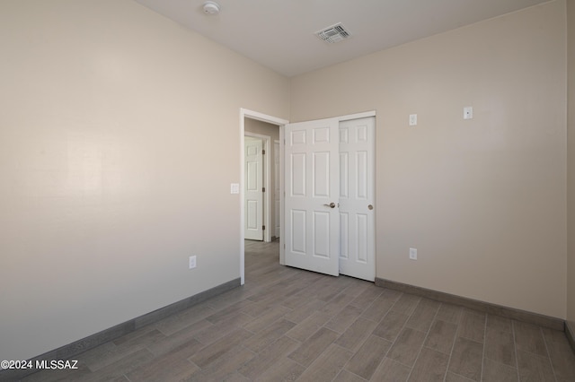 unfurnished bedroom featuring baseboards, a closet, wood finished floors, and visible vents