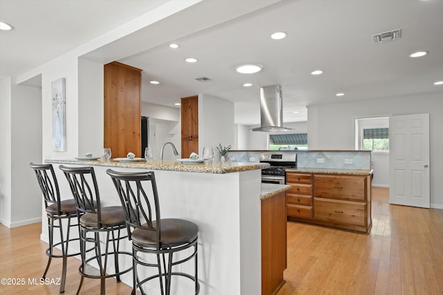 2350 E Juanita St, Tucson, AZ 85719 - kitchen with gas stove, island exhaust hood, brown cabinets, a peninsula, and tasteful backsplash