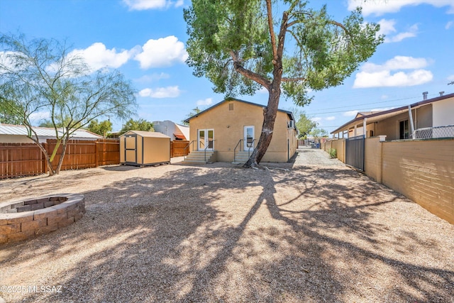 rear view of house with a storage unit, stucco siding, a fenced backyard, an outdoor fire pit, and an outdoor structure