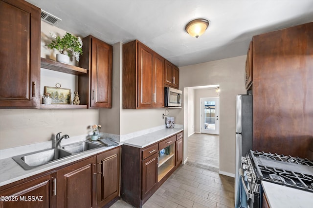 kitchen featuring visible vents, open shelves, appliances with stainless steel finishes, light wood-style floors, and a sink