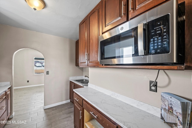 kitchen with baseboards, wood tiled floor, a sink, stainless steel microwave, and brown cabinets