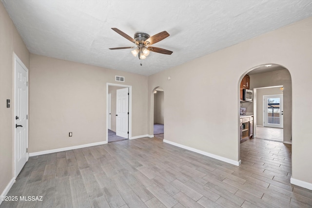 spare room featuring visible vents, a ceiling fan, wood finished floors, arched walkways, and baseboards