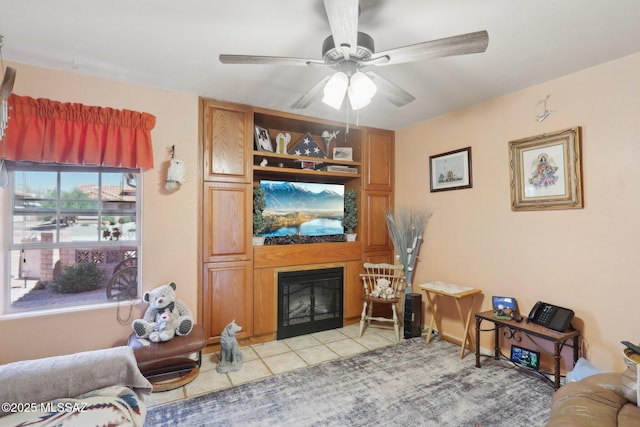 living area with light tile patterned floors, a glass covered fireplace, and ceiling fan