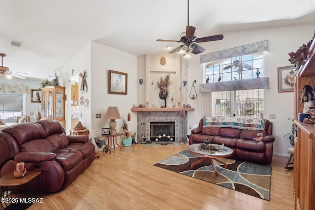 living area with high vaulted ceiling, a tile fireplace, wood finished floors, visible vents, and ceiling fan