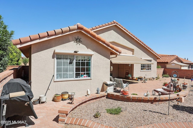 view of front facade featuring stucco siding, a tile roof, fence, and a patio area