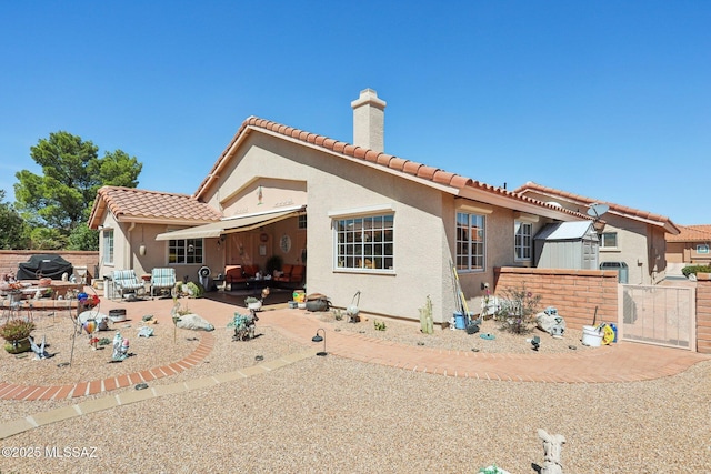exterior space featuring stucco siding, a tiled roof, a gate, a patio area, and a chimney