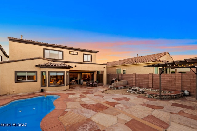 back of house at dusk with a tiled roof, a fenced backyard, stucco siding, and a patio area